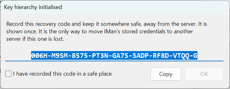 The Key hierarchy initialised window. It asks you to record the recovery code and keep it somewhere safe, away from the server, because it is shown once and is the only way to move IMan's stored credentials to another server if this one is lost. Below it are an example recovery code of eight groups of four characters and a check character, a tick box "I have recorded this code in a safe place", a Copy button and an OK button that is unavailable until the box is ticked